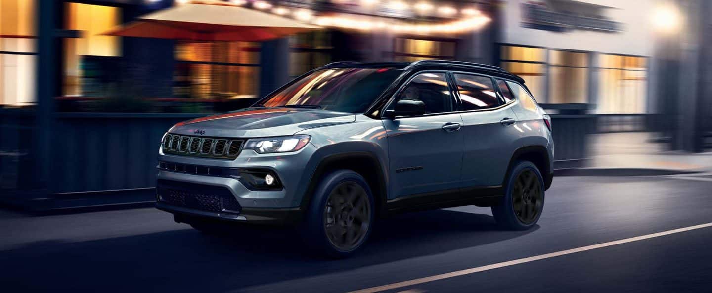 Un Jeep Compass Limited Altitude plateado del año 2026 circulando por una calle de la ciudad de noche, con el fondo desenfocado para indicar que el vehículo está en movimiento.