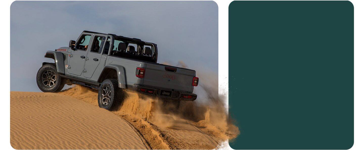 Una Jeep Gladiator Mojave X 2026 gris trepando una colina de arena en el desierto.
