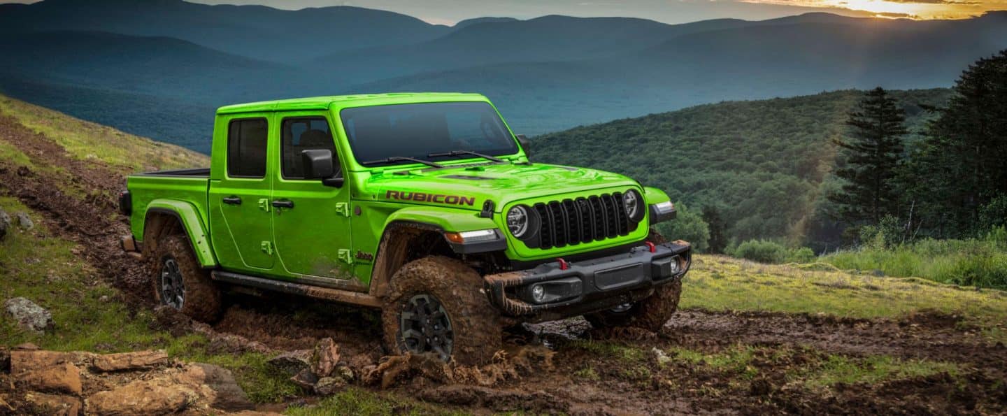 Un Jeep Gladiator Rubicon X 2026 de color verde lima avanzando penosamente por un sendero embarrado todoterreno, en las montañas.