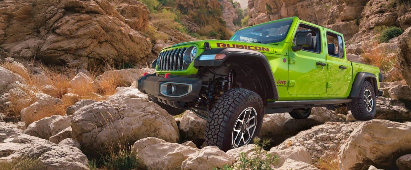 Un Jeep Gladiator Rubicon 2026 verde lima, sin capota, avanzando lentamente sobre rocas en un sendero todoterreno extremo.