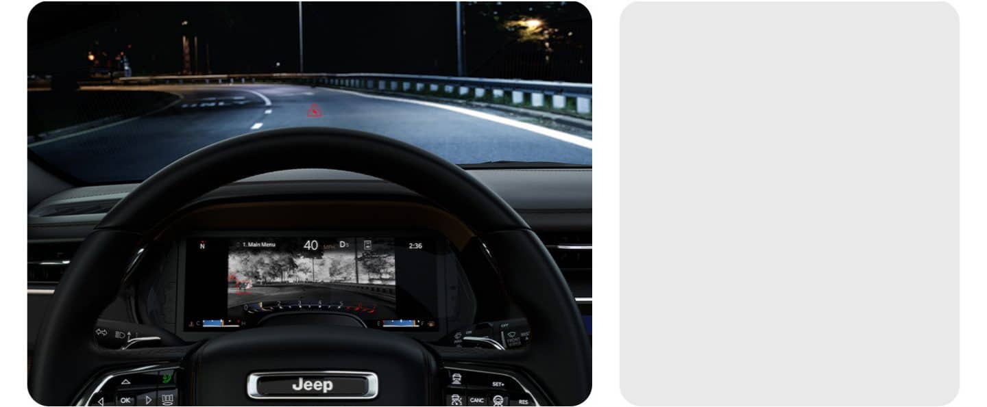 Una carretera oscura adelante, visible a través del parabrisas del Jeep Grand Cherokee 2026, mientras la pantalla digital muestra una imagen térmica de la misma carretera con un venado de pie al lado que no se puede observar a simple vista.