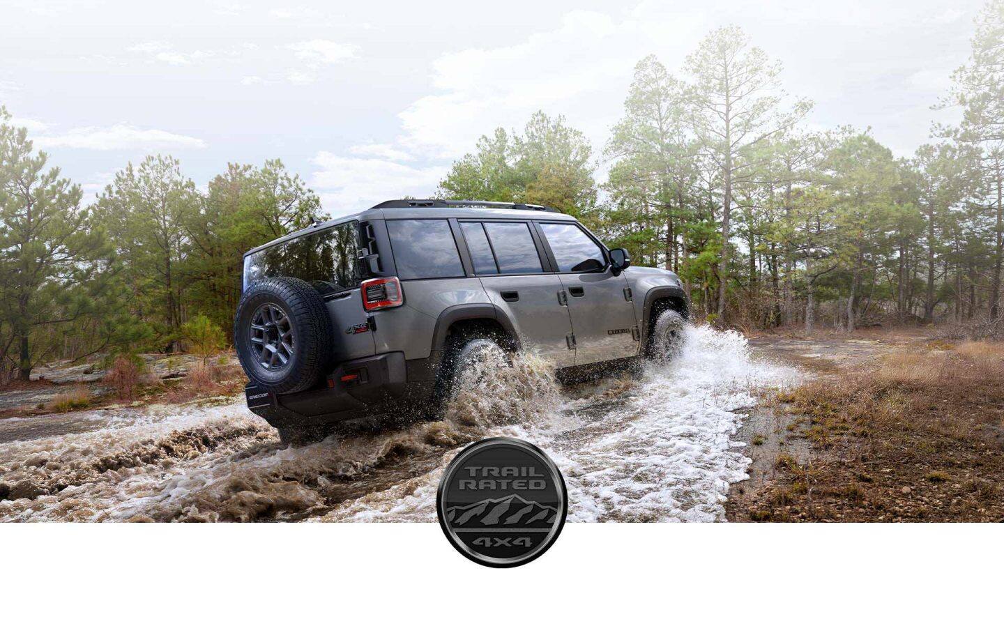 Ángulo trasero del lado del pasajero de un Jeep Recon Moab 2026 gris vadeando un arroyo fangoso. El emblema Trail Rated 4x4.