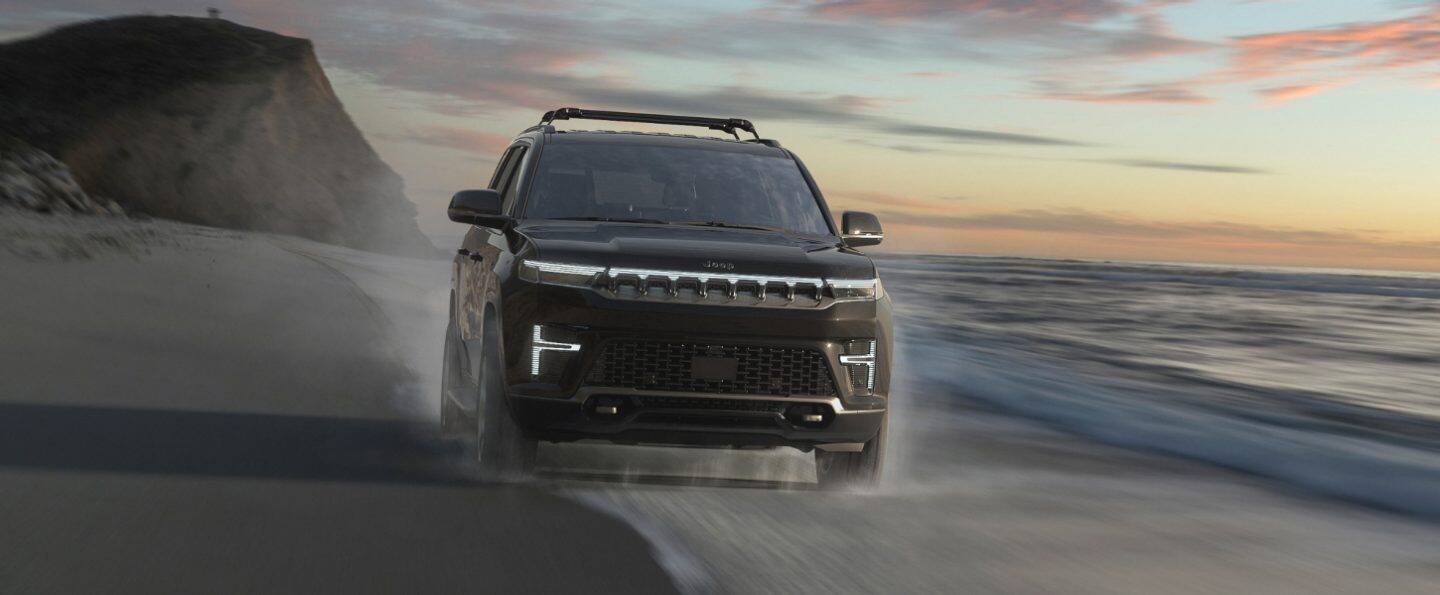 Una Jeep Grand Wagoneer Summit Obsidian 2026 blanca circulando por una carretera cubierta de nieve en la montaña.