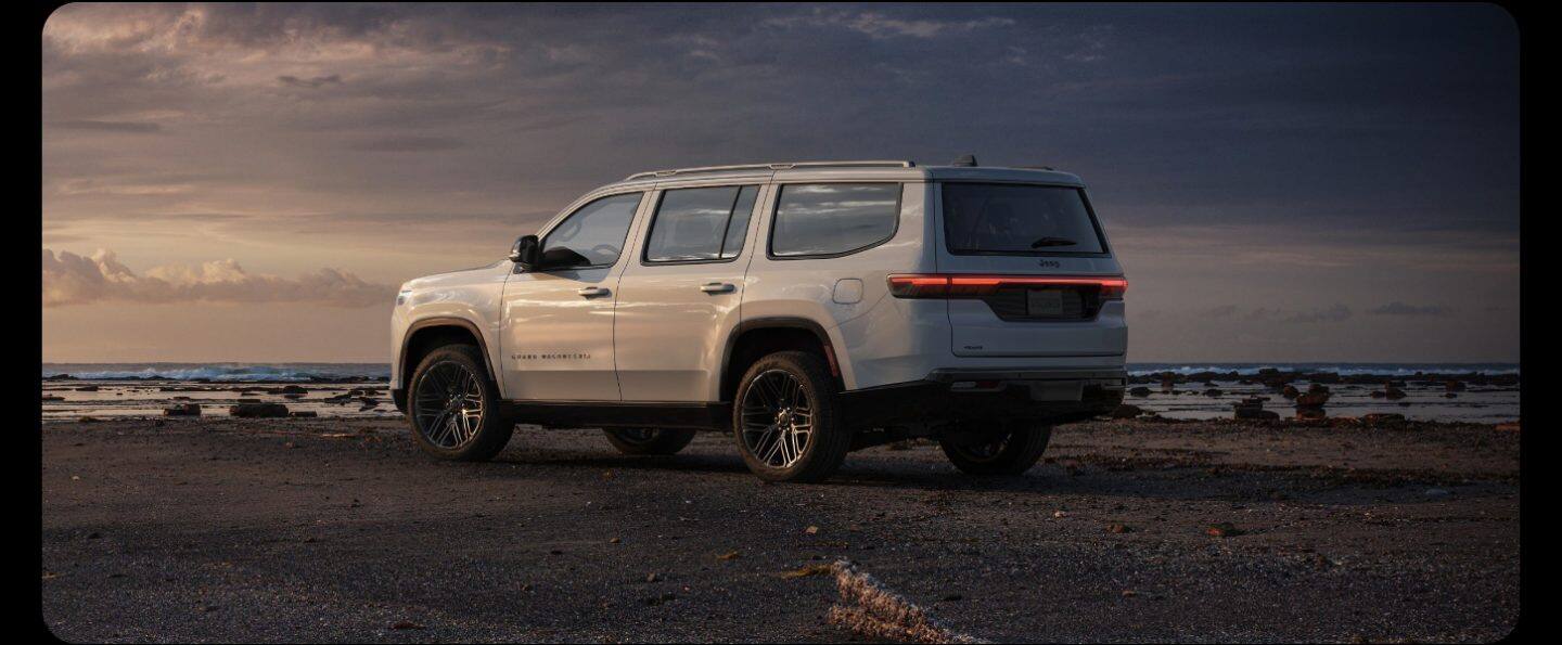 Perfil en ángulo del lado del conductor de un Jeep Grand Wagoneer Summit Reserve Obsidian azul 2026 estacionado al costado de una carretera en las montañas