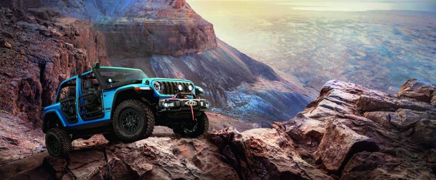 Un Jeep Wrangler Rubicon 2026 verde lima de cuatro puertas, ingresando a un arroyo fuera de la carretera, salpicando agua mientras avanza.