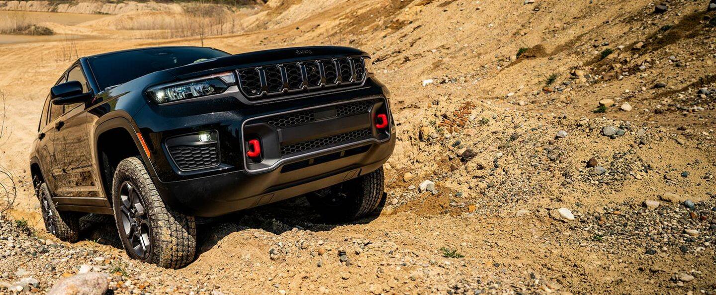 Una Jeep Grand Cherokee Trailhawk 2027 negro subiendo por una colina todoterreno arenosa llena de surcos.