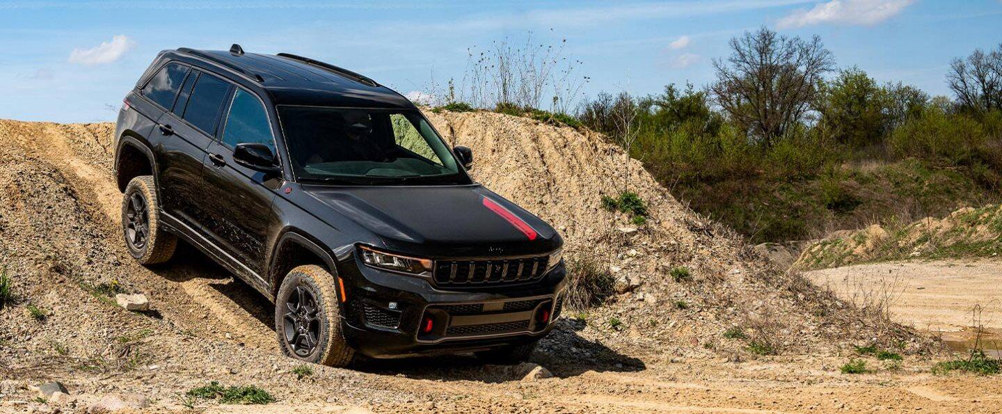 Una Jeep Grand Cherokee Trailhawk 2027 negra bajando por un sendero todoterreno arenoso.