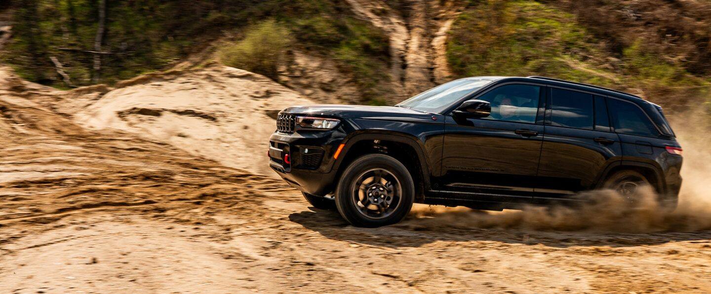 Una Jeep Grand Cherokee Trailhawk 2027 negro subiendo por un sendero todoterreno arenoso.