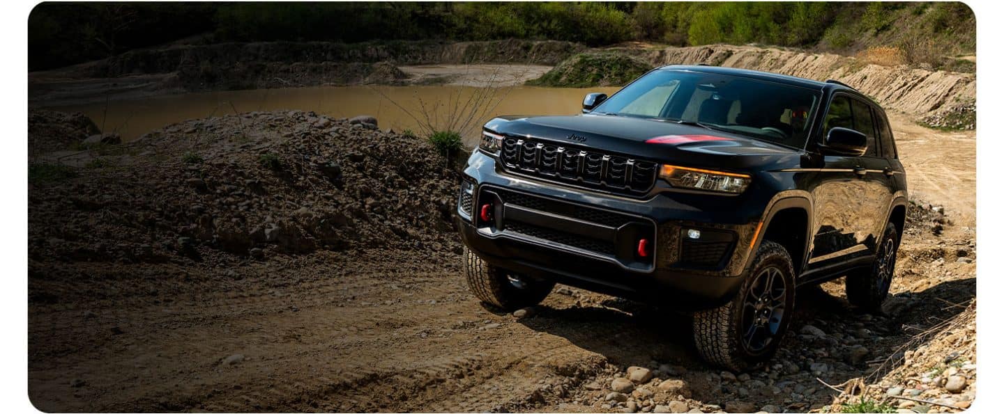 Una Jeep Grand Cherokee Trailhawk 2027 negra subiendo por una colina todoterreno arenosa.