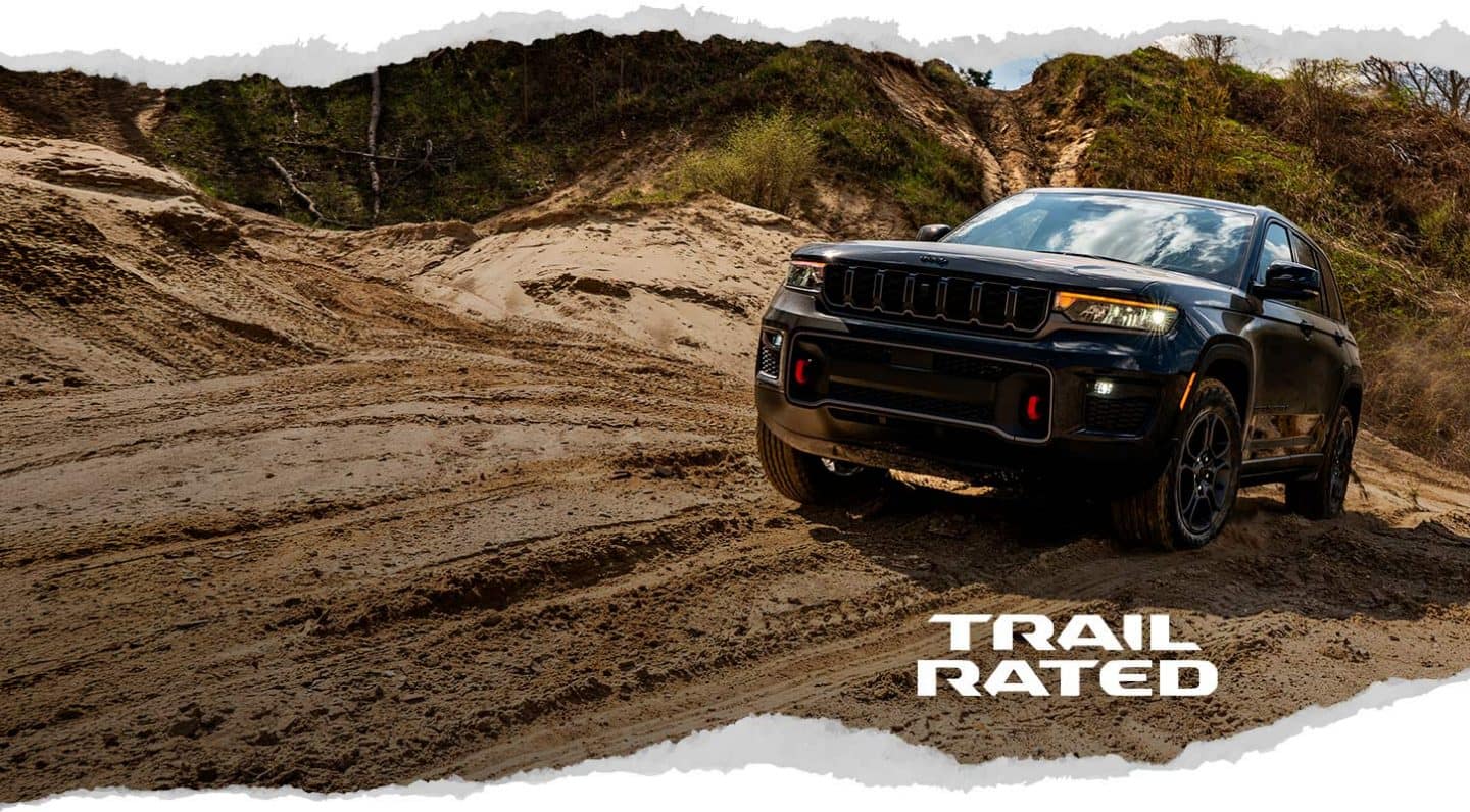 Una Jeep Grand Cherokee Trailhawk 2027 Black subiendo por un sendero arenoso fuera del camino. Trail Rated.