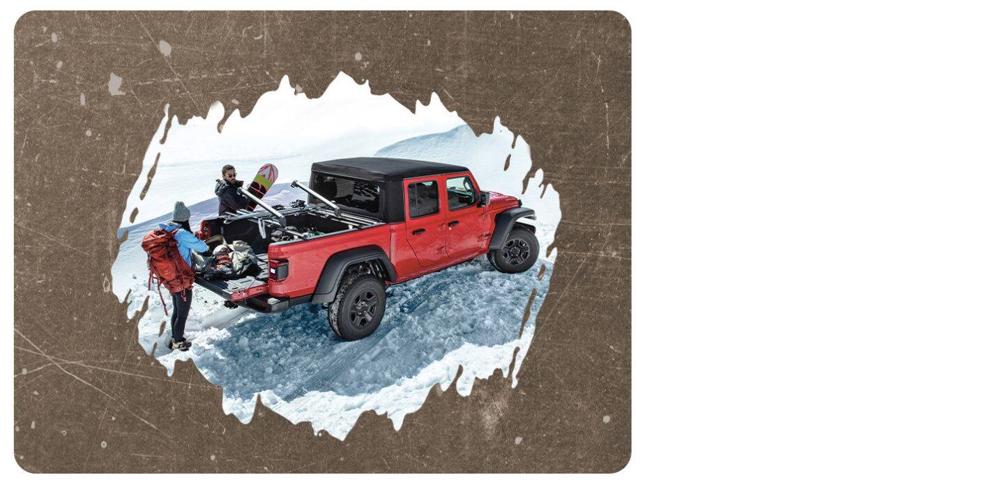 A red 2025 Jeep Gladiator Sport with a black roof, parked on snow, its tailgate open and a couple taking ski gear out of the pickup bed.