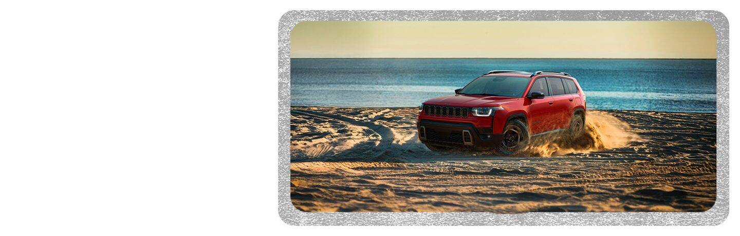 A red 2026 Jeep Cherokee Limited traveling on a beach, kicking up sand as it goes.