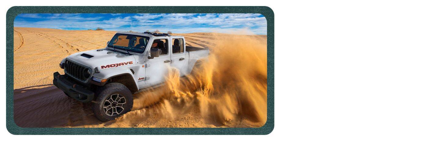 A white 2026 Jeep Gladiator Mojave X traveling through the desert, kicking up sand as it goes.
