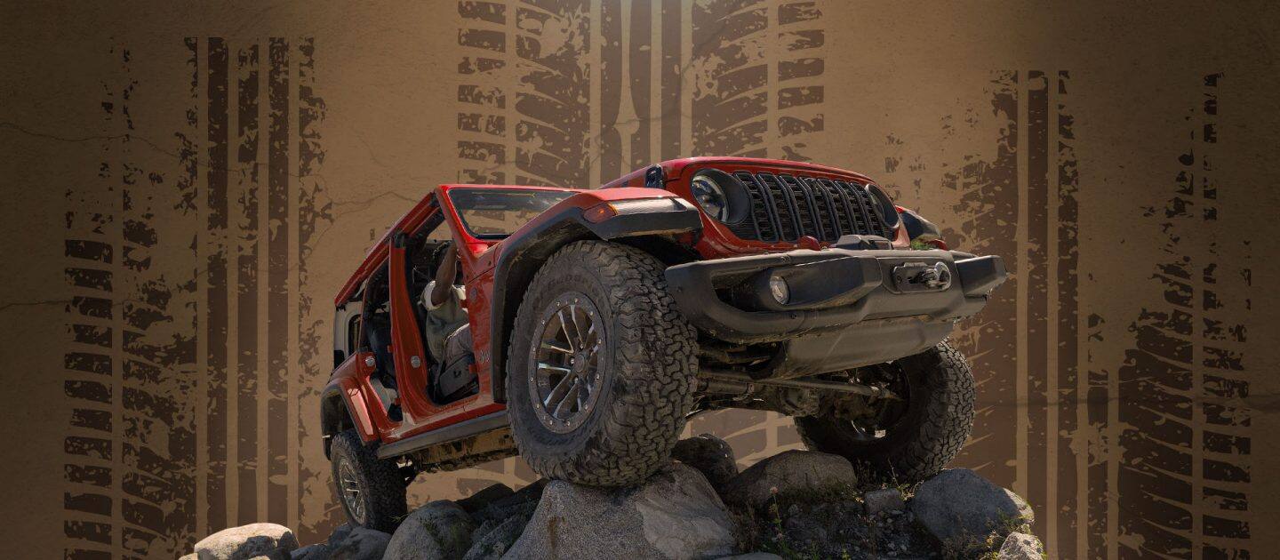Un Jeep Wrangler Rubicon X 2026 rojo con neumáticos grandes. Con las puertas y el techo desmontados, mientras trepa por una colina de rocas. Toma desde un ángulo bajo.