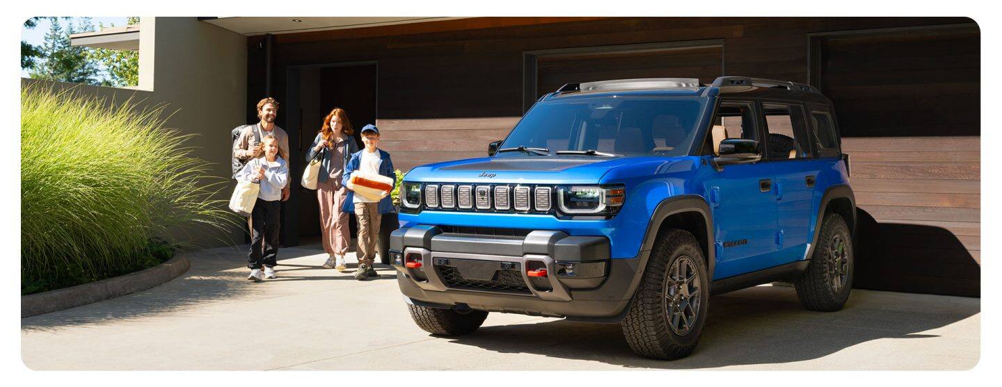 Una Jeep® Recon Moab 2026 azul estacionada en la entrada de una casa contemporánea, mientras una familia de cuatro integrantes camina hacia la SUV.
