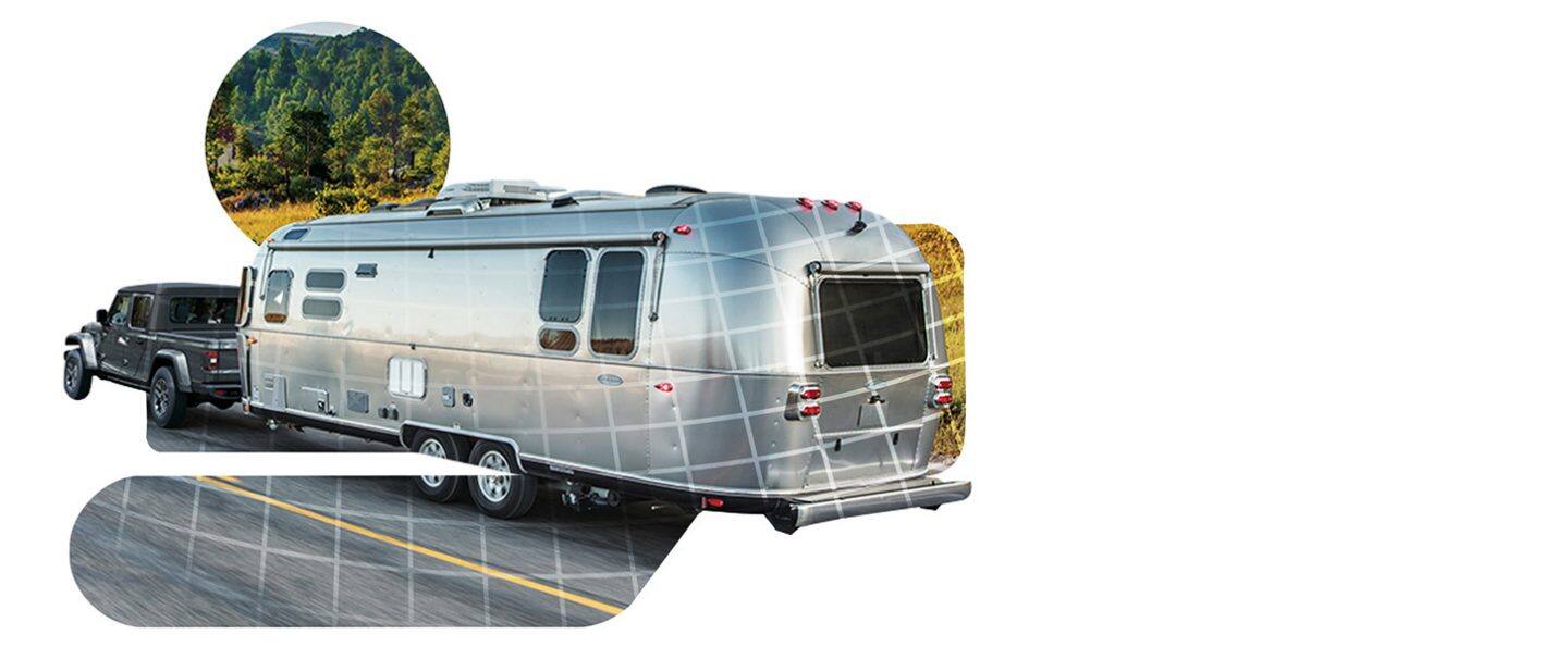 A dark gray 2026 Jeep Gladiator Sport S traveling down a highway, towing a large travel trailer.