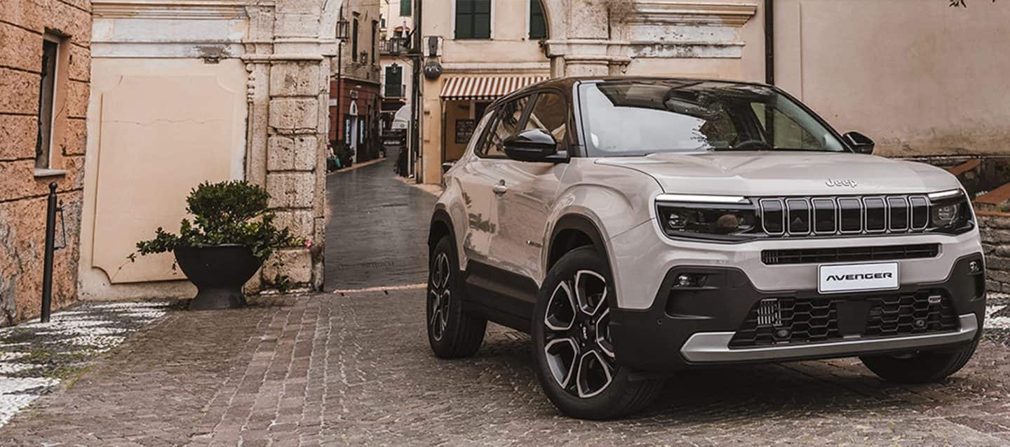 Bijeli 2023 Jeep Wrangler Rubicon 4xe i limeta zeleni 2023 Jeep Gladiator Rubicon, oba s uklonjenim vratima i krovom, parkirani jedan nasuprot drugog na pijesku u podnožju velikog, stjenovitog brda. Prodajni događaj za Dan sjećanja.