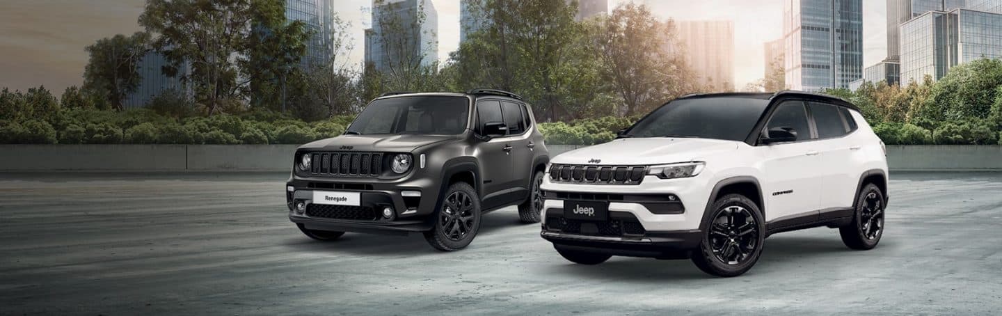 A white 2023 Jeep Wrangler Rubicon 4xe and a lime green 2023 Jeep Gladiator Rubicon, both with their doors and roofs removed, parked opposite of each other on sand at the foot of a large, rocky hill. Memorial Day Sales Event.