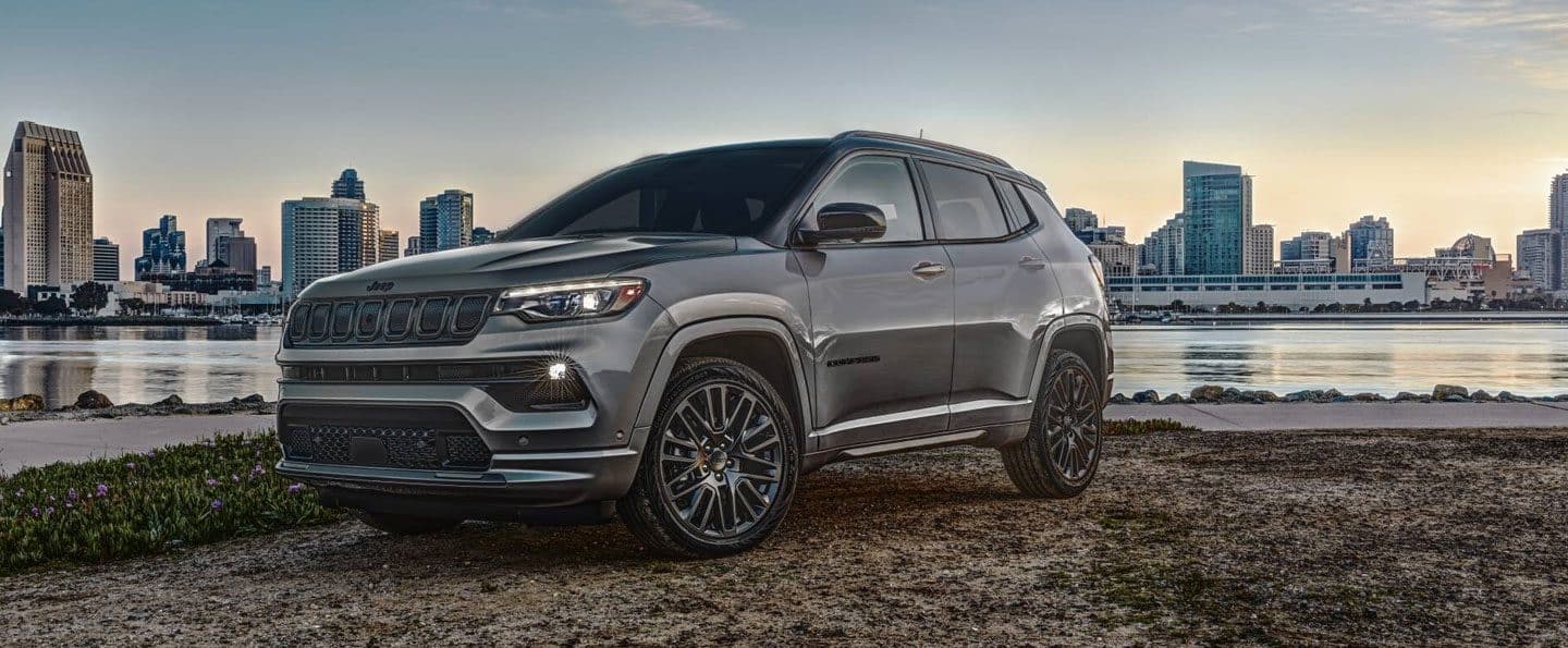 Un angle surélevé d’un Jeep Compass Trailhawk 2023 bleu garé hors route. Compass. Le logo de l'événement de vente du Memorial Day.