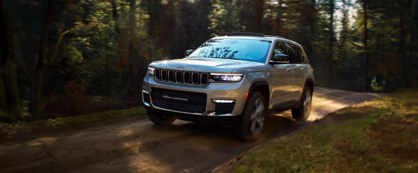 Белый 2023 Jeep Wrangler Rubicon 4xe и зеленый 2023 Jeep Gladiator Rubicon, со снятыми дверями и крышами, припаркованы друг напротив друга на песке у подножия большого скалистого холма. Мероприятие по продаже в день памяти.