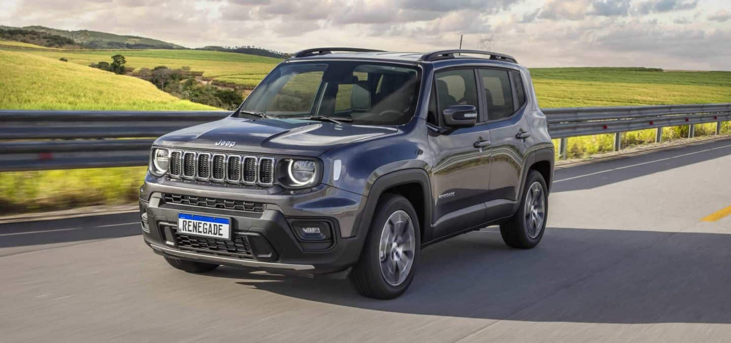 A blue gray 2023 Jeep Renegade Trailhawk fording through a narrow creek off-road, with water spraying above the vehicle's wheel wells. Renegade.