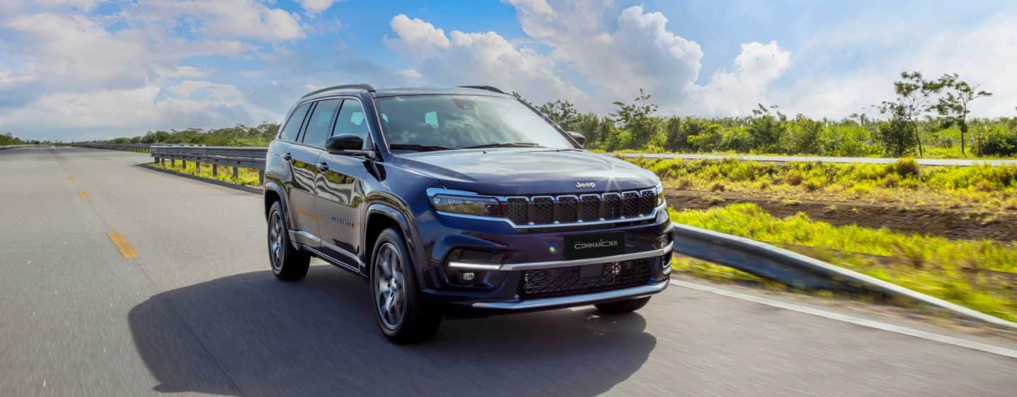 A 2023 Jeep Cherokee Altitude Lux being driven on road beside a lake with an overcast sky and the background blurred to indicate the vehicle is in motion.