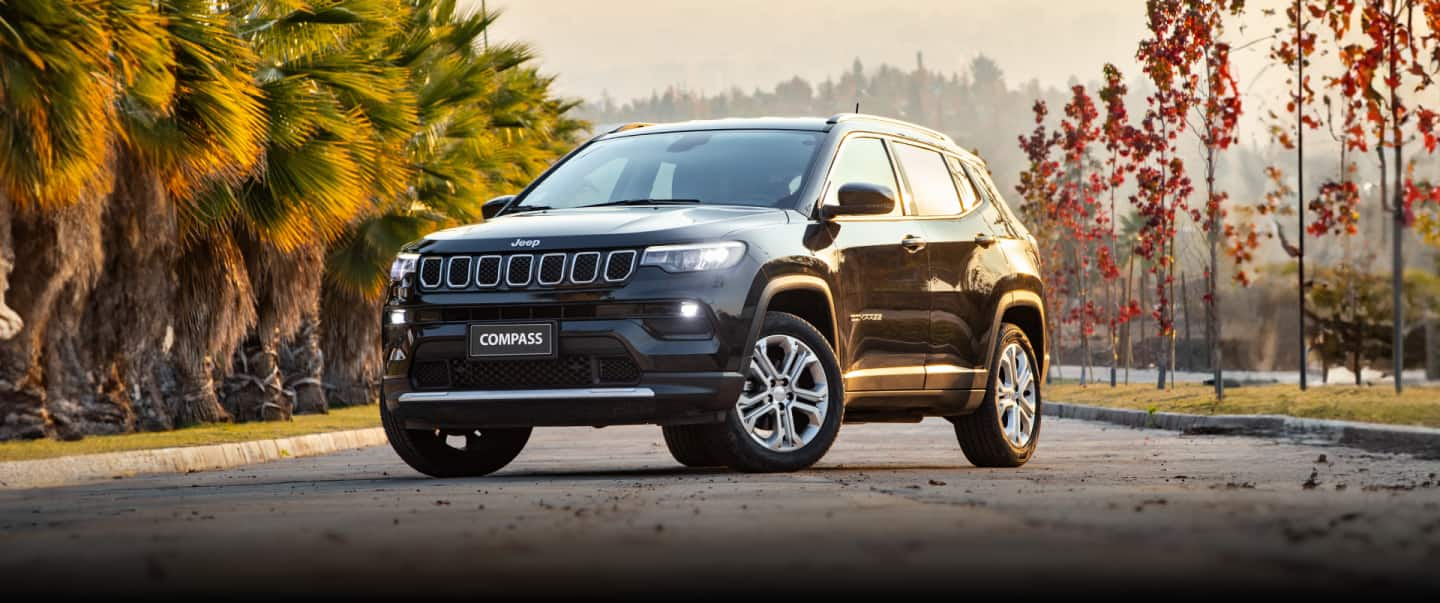 A rear view of a 2023 Jeep Compass High Altitude being driven on a winding highway during a rainstorm.