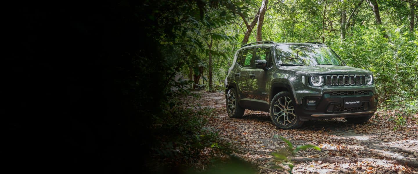 A yellow 2023 Jeep Renegade Trailhawk parked on a rocky outcrop in the woods.