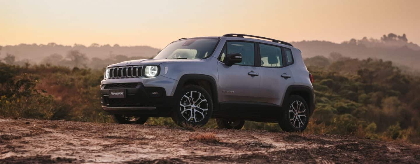 A head-on view of the 2023 Jeep Renegade Limited being driven on a busy city street at sunset, with its headlamps on.