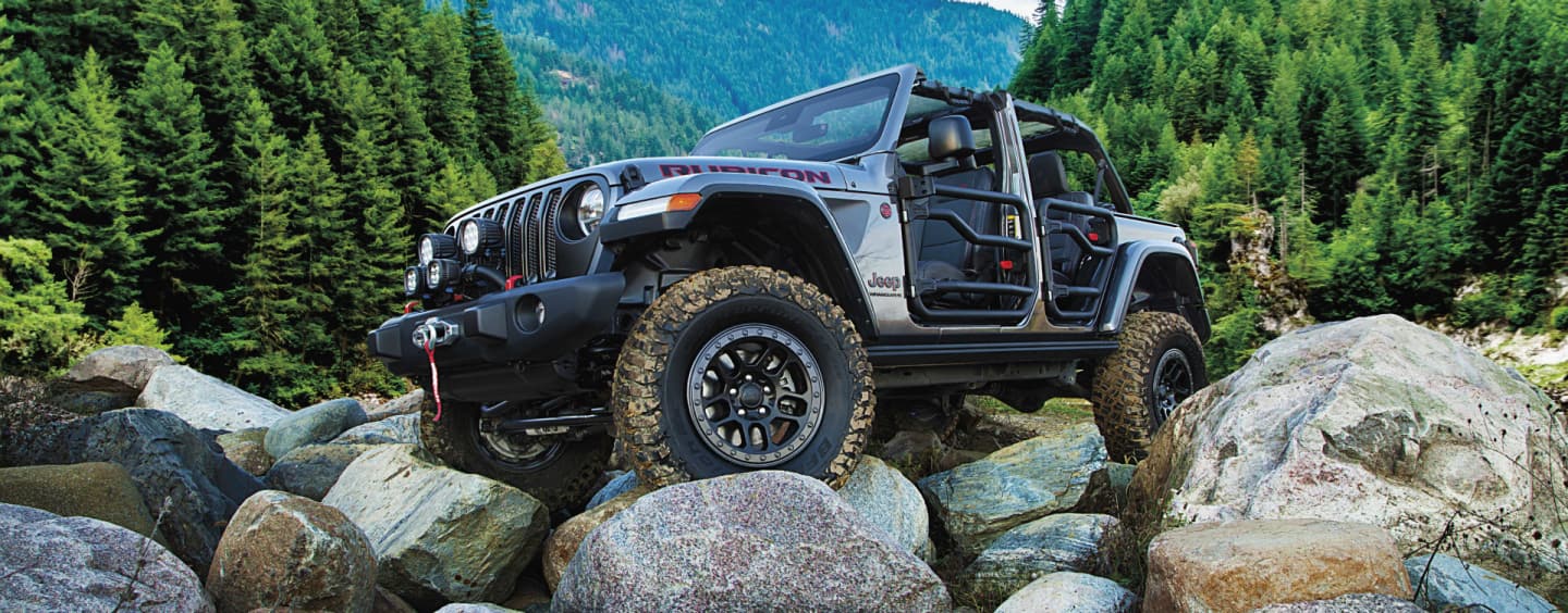 A red 2023 Jeep Wrangler Rubicon 4xe with its roof and doors removed, being driven down a steep hill off-road. Wrangler.