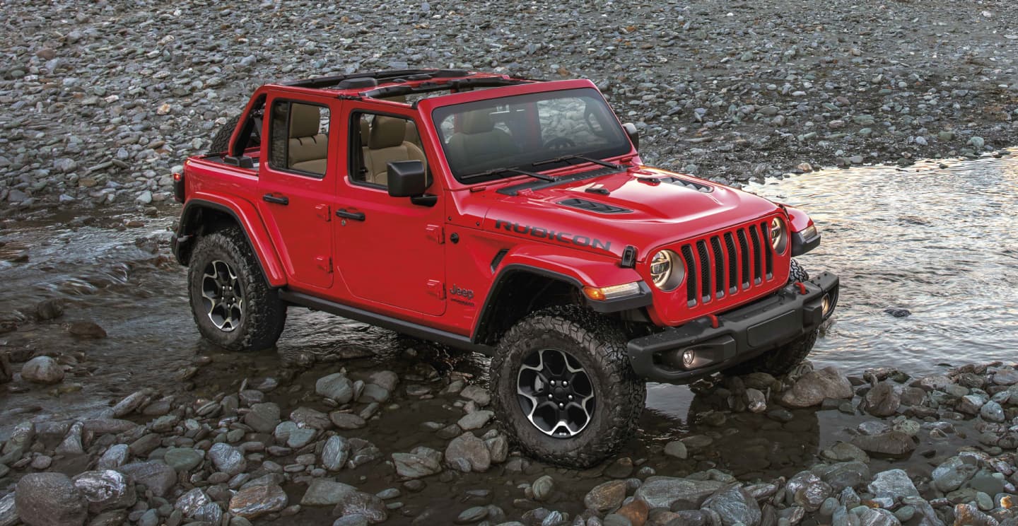 The 2023 Jeep Wrangler Rubicon 4xe being driven through a shallow stream with its doors and roof off.