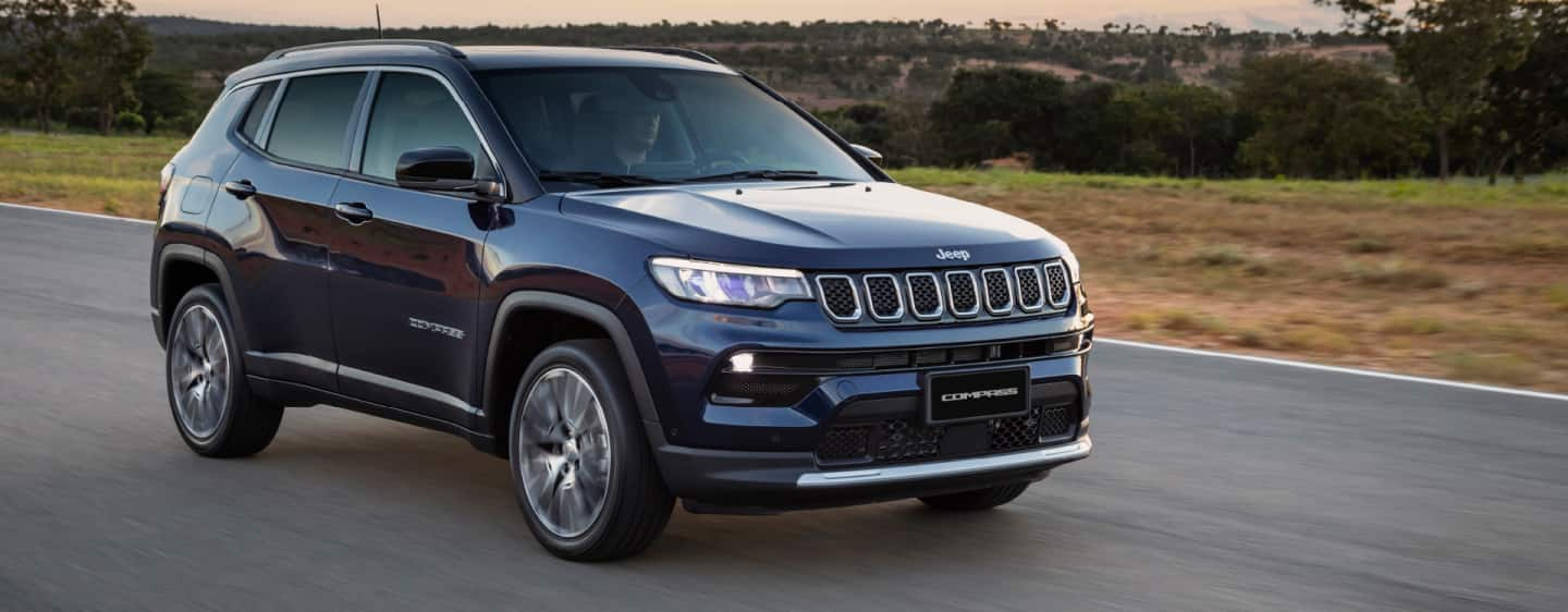 A raised head-on view of a 2023 Jeep Compass Trailhawk being driven off-road through a wooded trail.