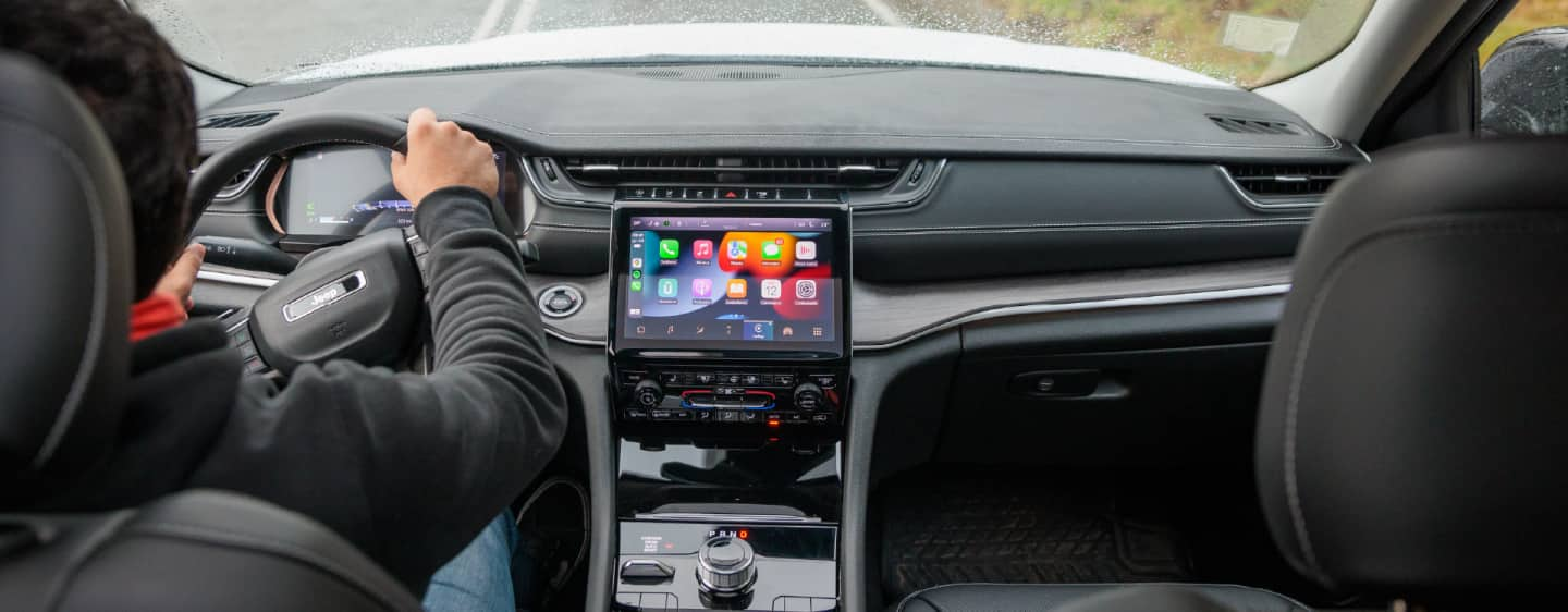 The cockpit of the 2023 Jeep Grand Cherokee Summit Reserve with a view of a lake at sunset through the windshield.