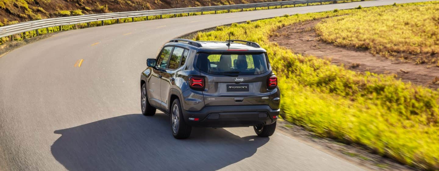 A head-on view of the 2023 Jeep Renegade Limited being driven on a busy city street at sunset, with its headlamps on.