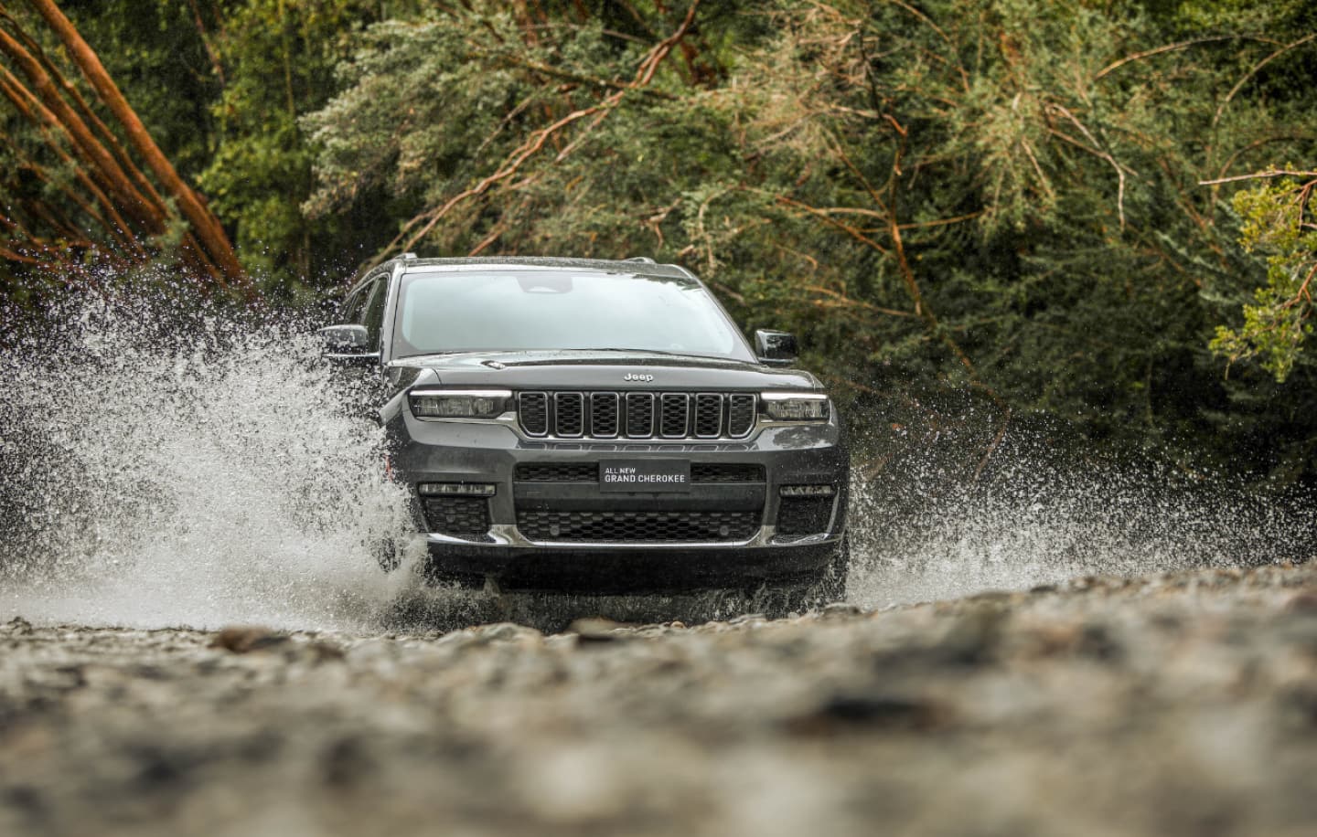 Una vista trasera de un Jeep Grand Cherokee Altitude negro de 2025 mientras cruza un arroyo.
