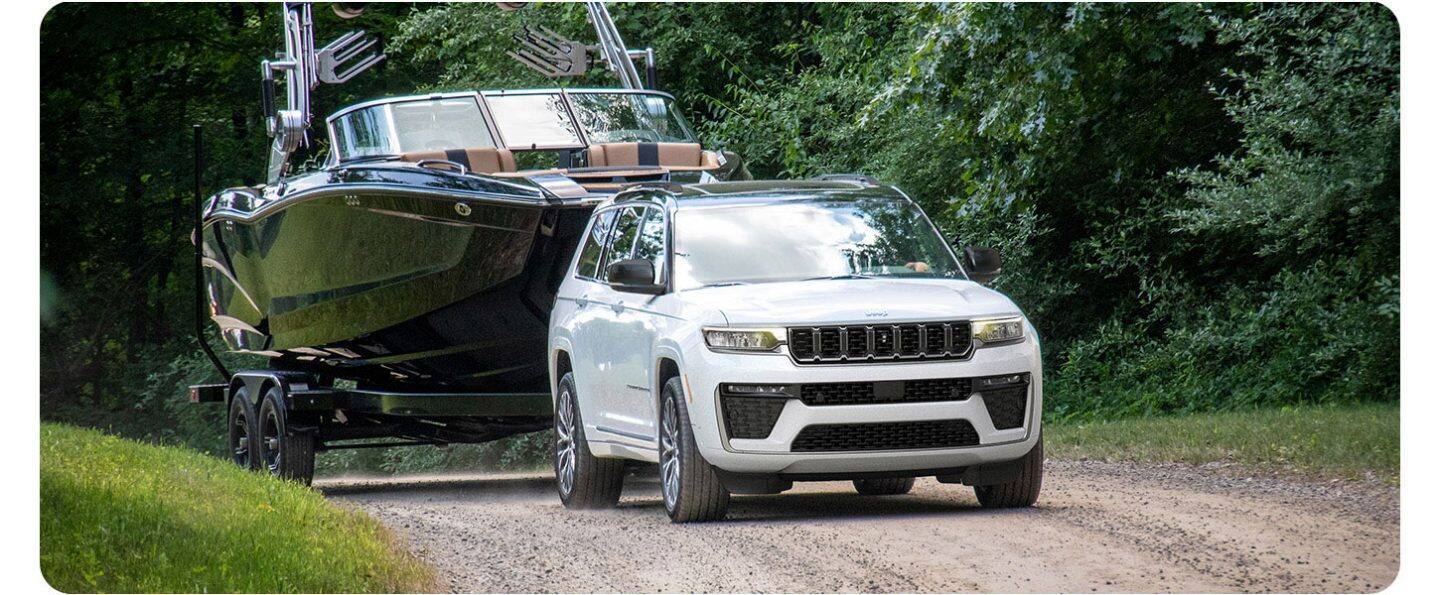 Un Jeep Grand Cherokee Summit 2026 blanco circulando por un camino de tierra, remolcando una lancha grande.