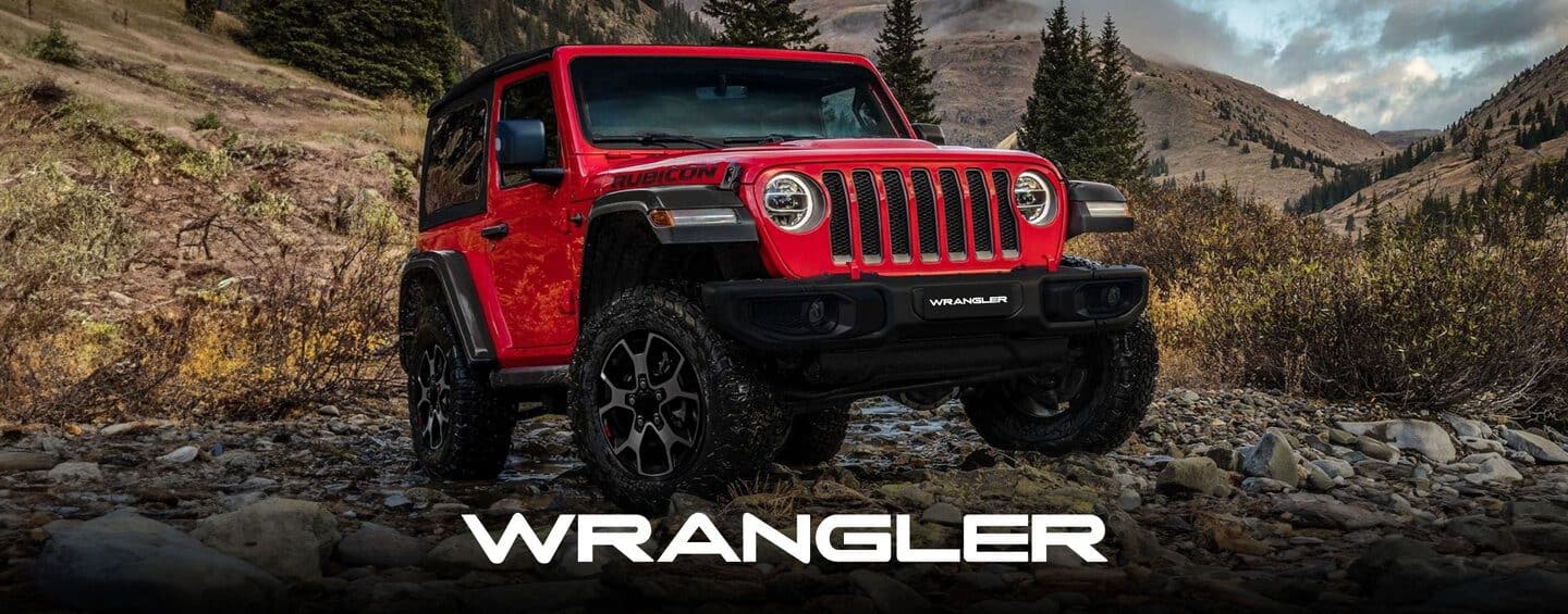 A 2024 Jeep Wrangler Rubicon 4xe with its doors and roof removed, being driven on a sandy trail off-road, with huge boulders on both sides.