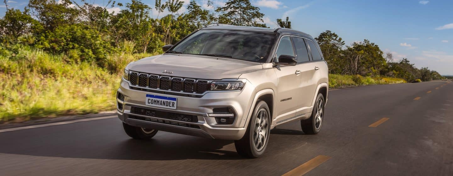 A 2023 Jeep Cherokee Altitude Lux being driven on road beside a lake with an overcast sky and the background blurred to indicate the vehicle is in motion.