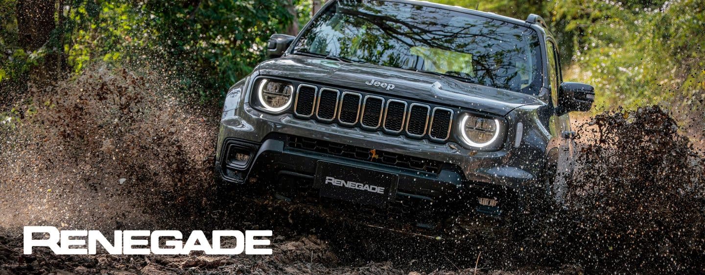 A blue gray 2023 Jeep Renegade Trailhawk fording through a narrow creek off-road, with water spraying above the vehicle's wheel wells. Renegade.