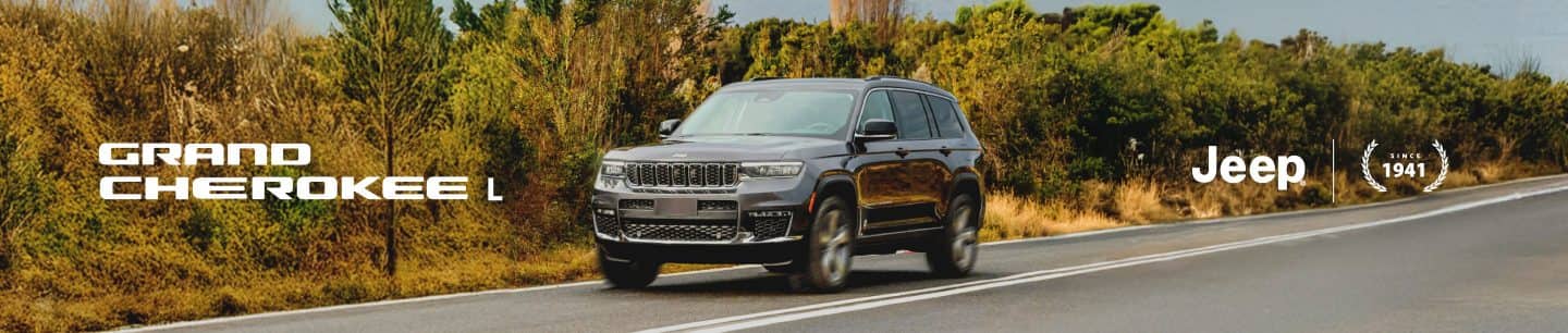 A profile of a 2022 Grand Wagoneer Obsidian with its headlamps on, parked on the pitcher's mound of a baseball field at night with a light beaming from the foggy background. Derek Jeter is walking in front of the vehicle.