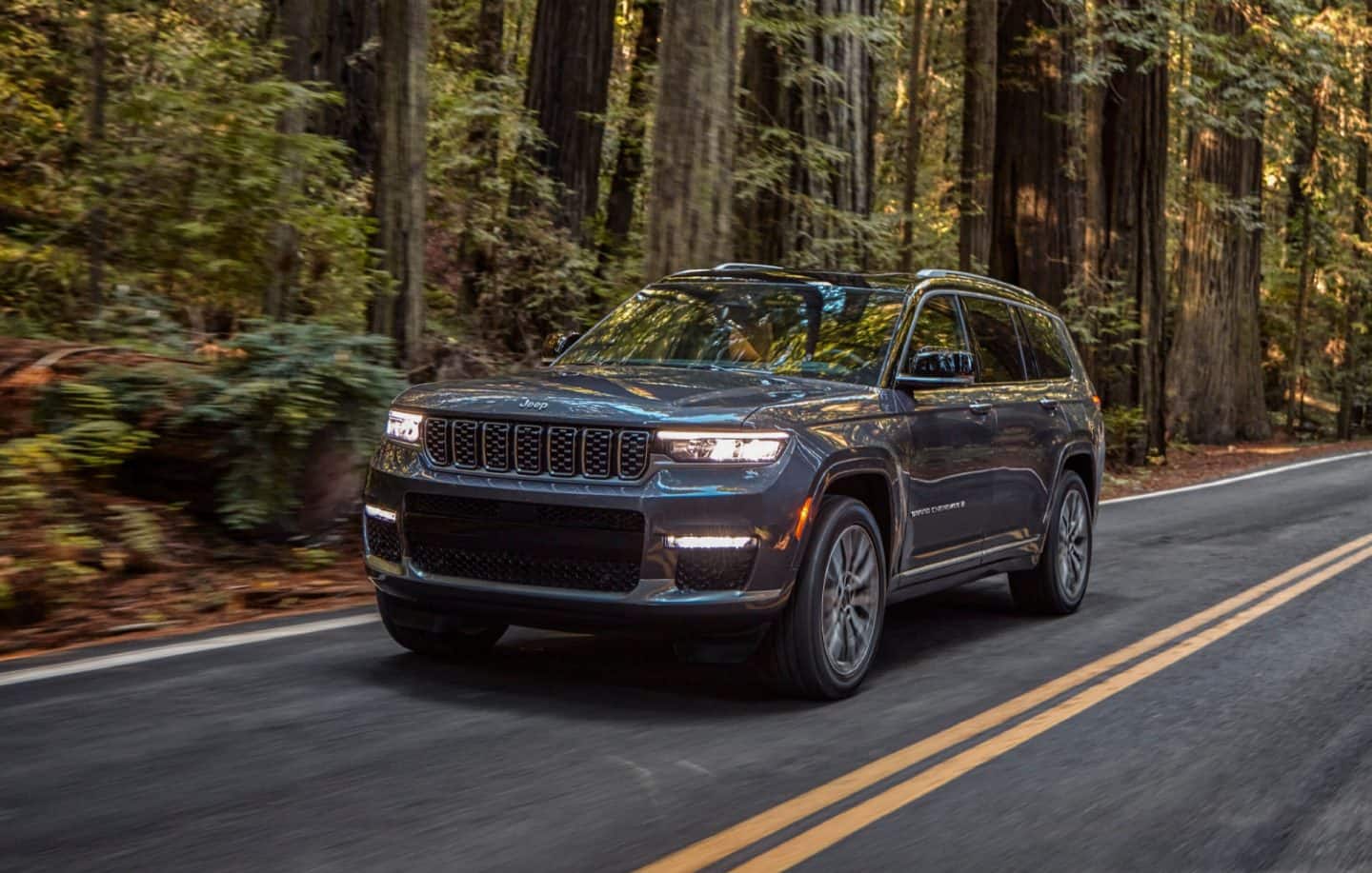 Una vista trasera de un Jeep Grand Cherokee L Altitude negro de 2023 mientras cruza un arroyo.