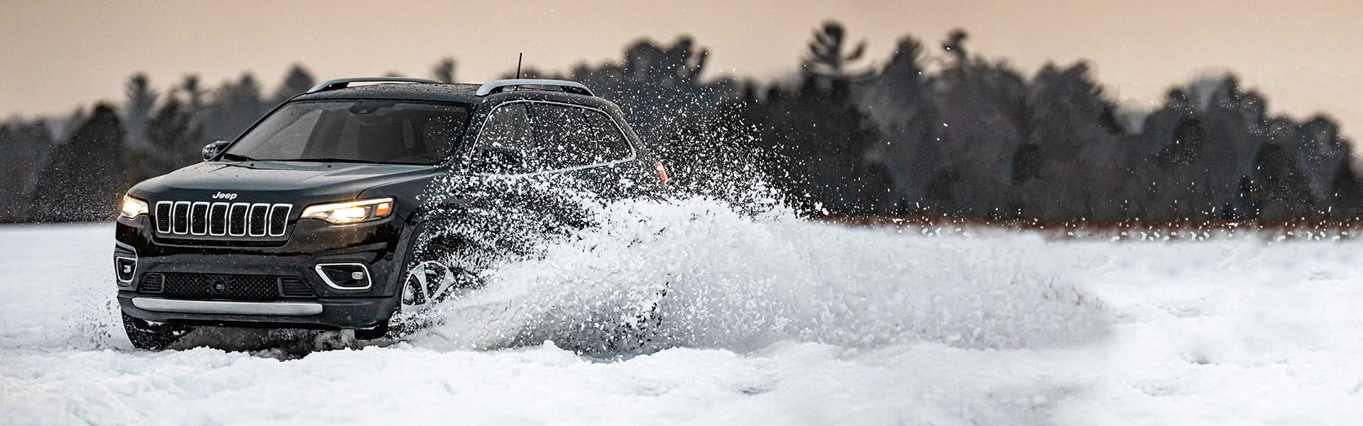 The 2021 Jeep Cherokee Limited being driven through snow, with a spray of loose snow coming from its wheels.