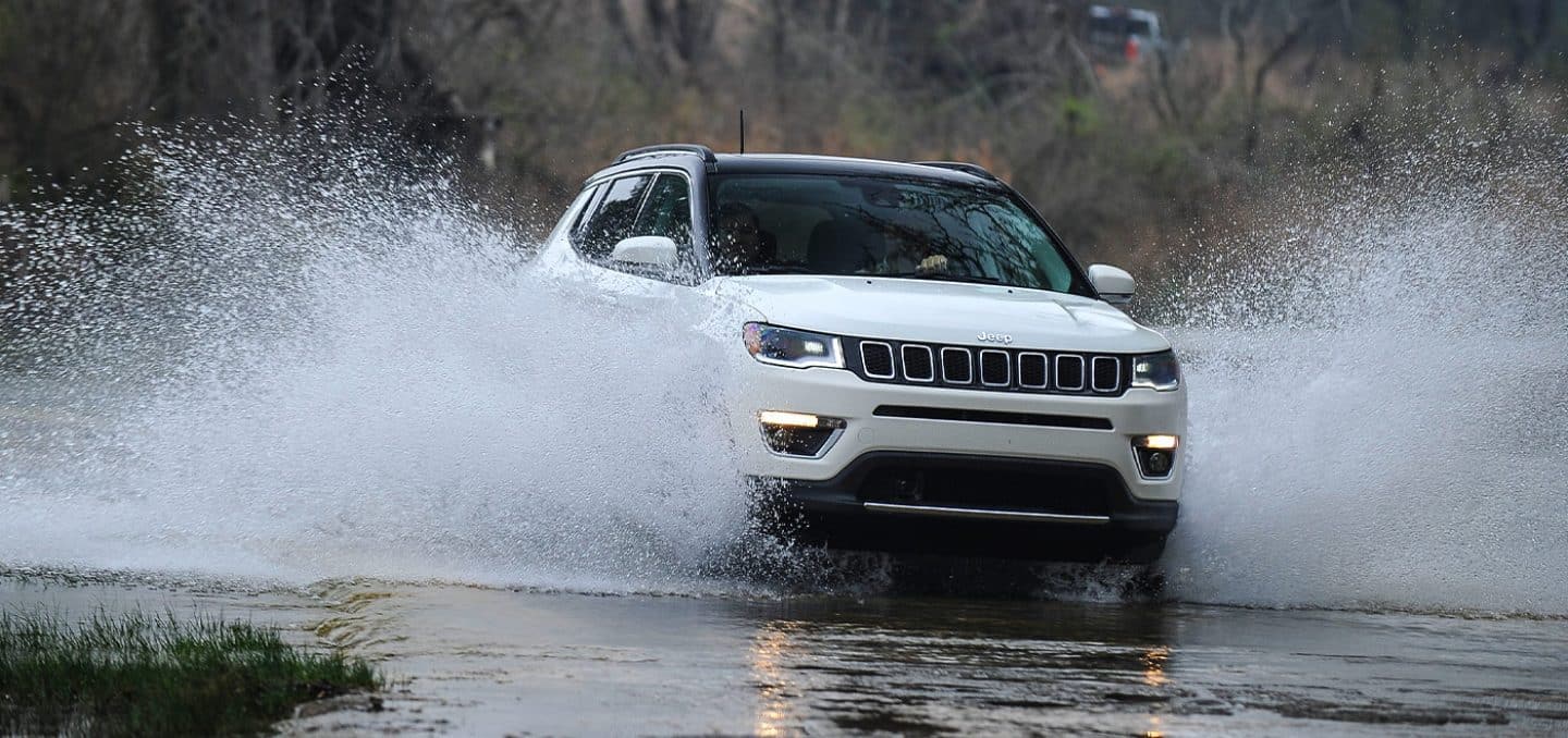 The 2021 Jeep Compass Limited spraying water from its wheels as it crosses a stream.
