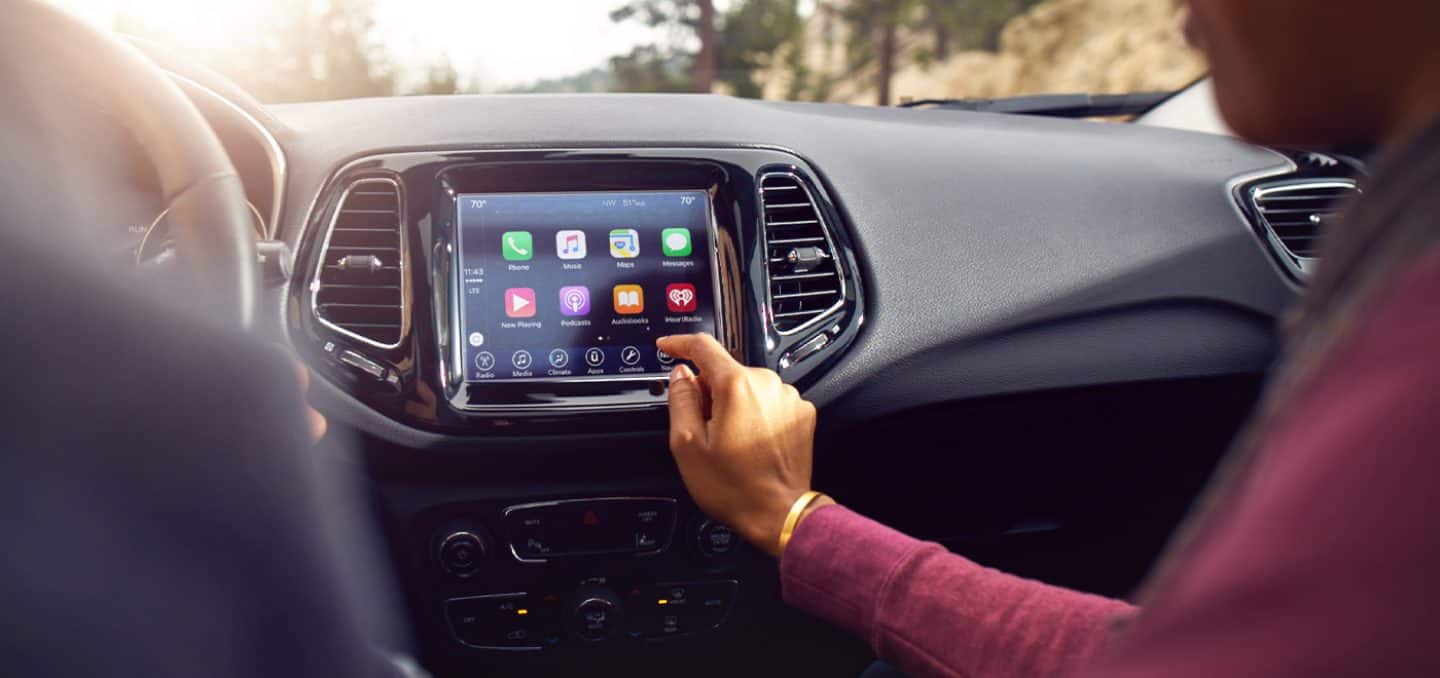 A close-up of the 8.4-inch touchscreen in the 2021 Jeep Compass Limited displaying several selections as a passenger taps the screen.