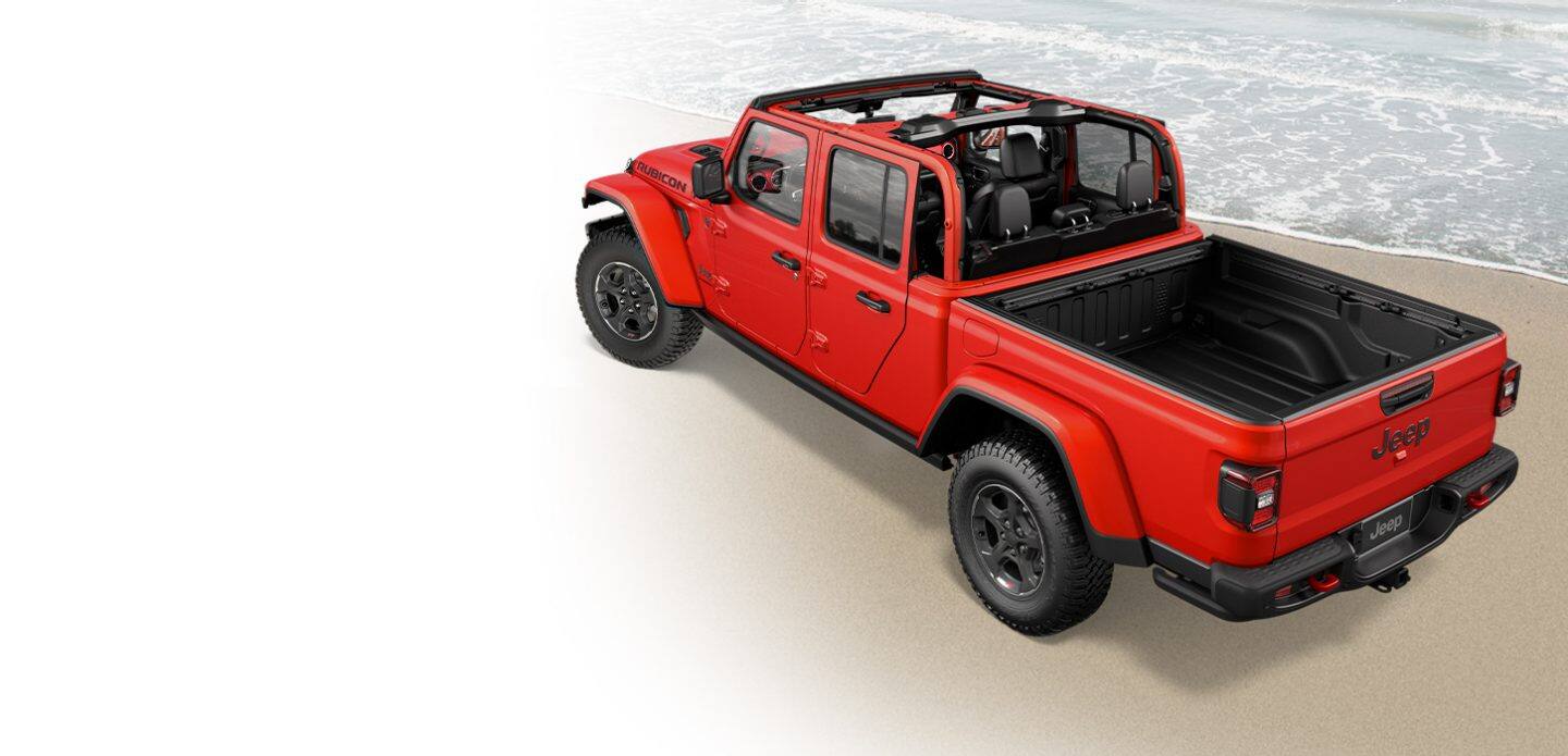 A red 2021 Jeep Gladiator Rubicon with no top, parked on a beach at the shoreline.