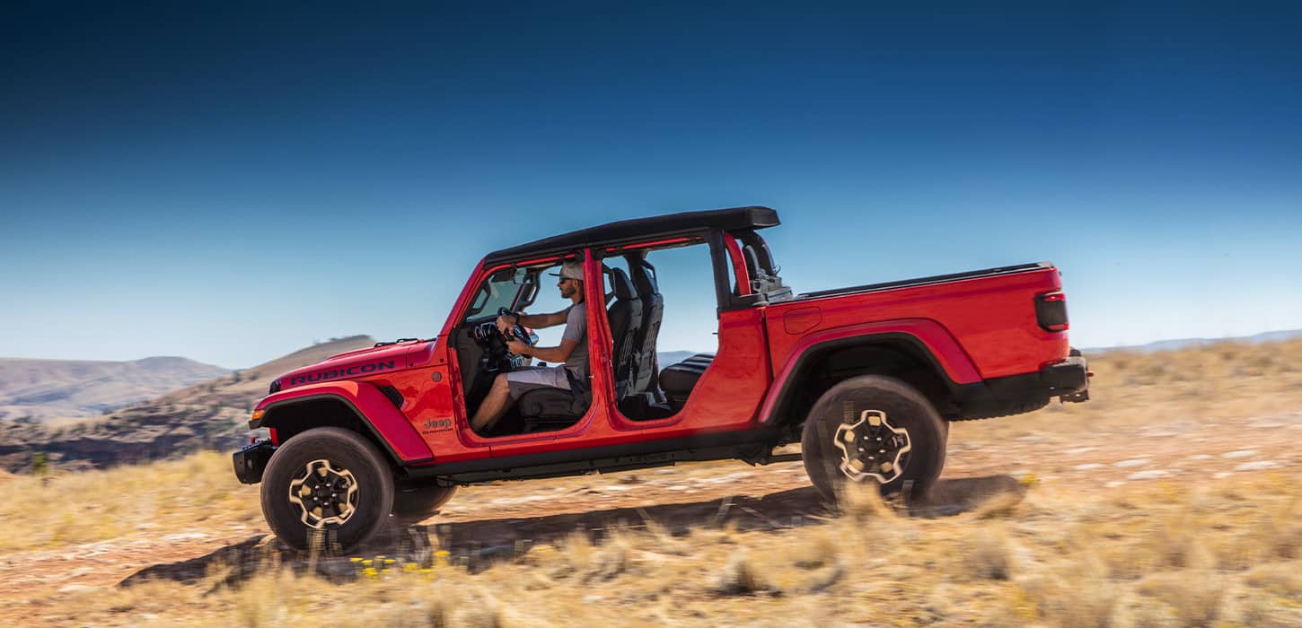A red 2021 Jeep Gladiator Rubicon being driven off-road with its doors off.