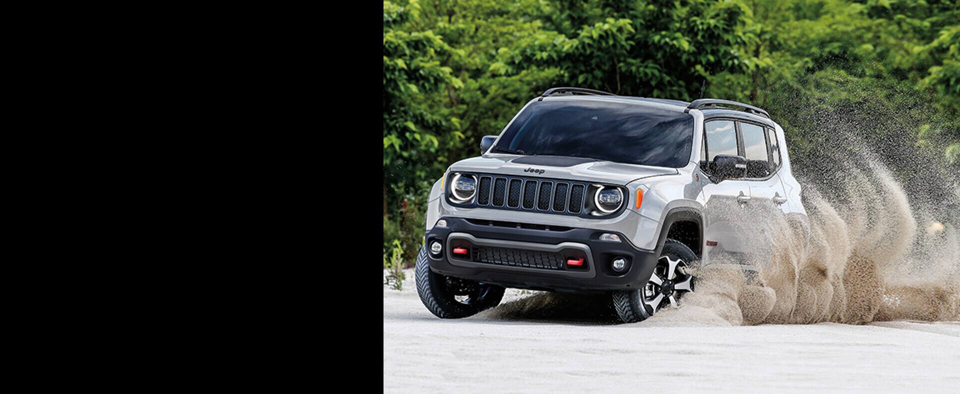 The wheels of 2021 Jeep Renegade throw up sand as it is driven on the beach.