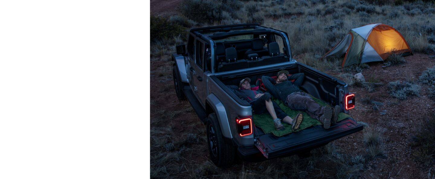 Two people lying full-length in the bed of the 2021 Jeep Gladiator Overland with the tailgate down, looking up at the stars.
