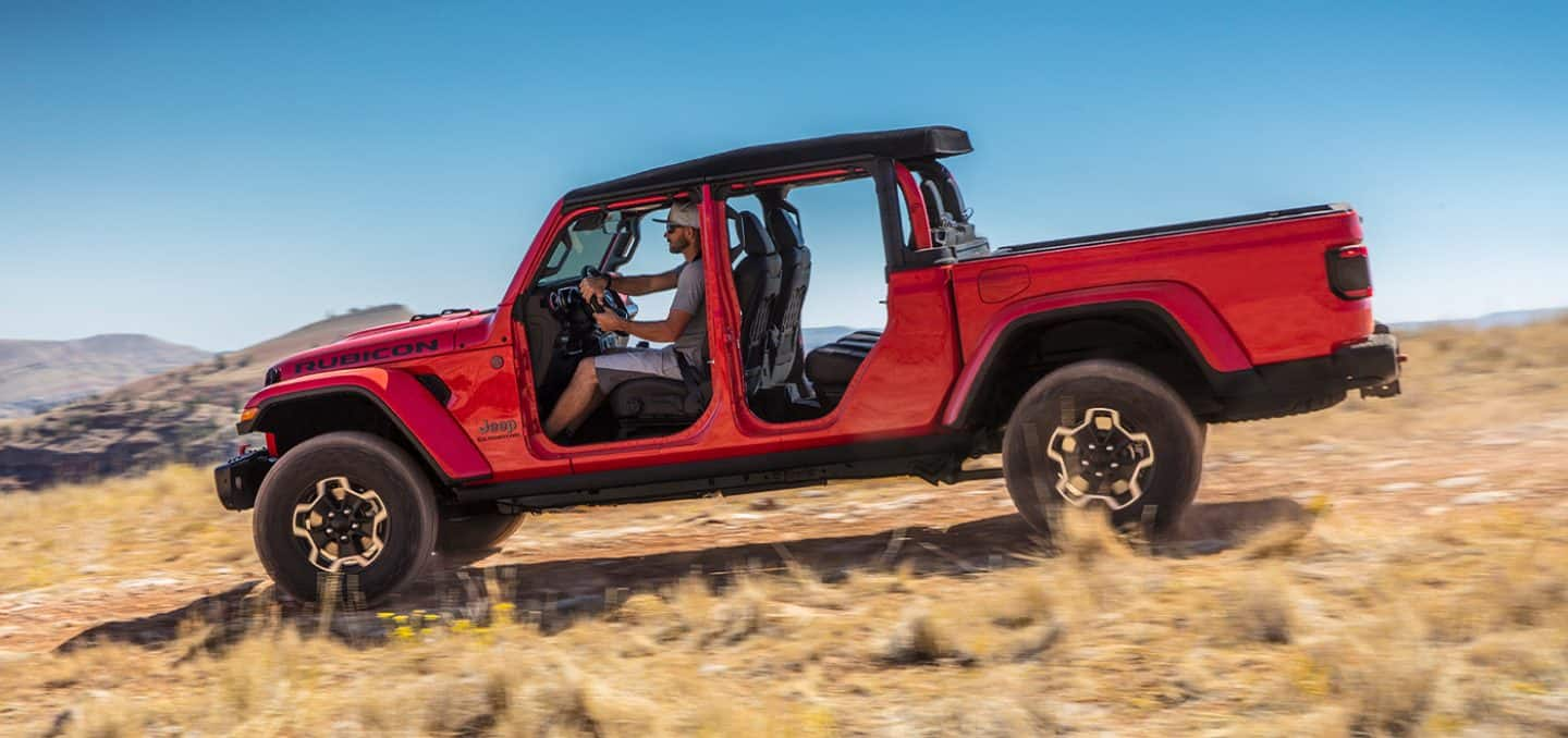 Display The 2021 Jeep Gladiator Rubicon being driven in a sandy field with all four doors removed.