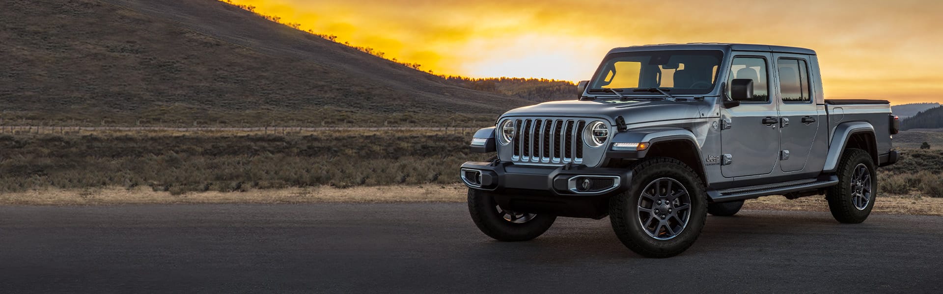 La Jeep Gladiator Overland 2021 estacionada al pie de una colina mientras el sol se oculta a la distancia.